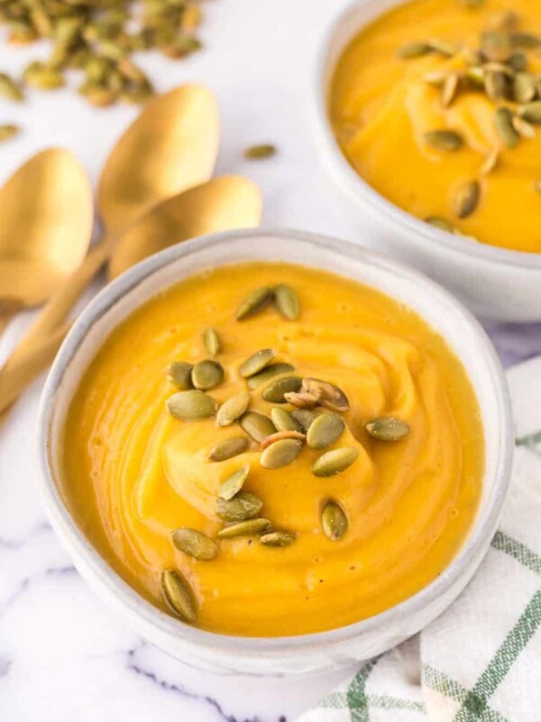 white serving bowls of roasted butternut squash soup with pumpkin seeds on top