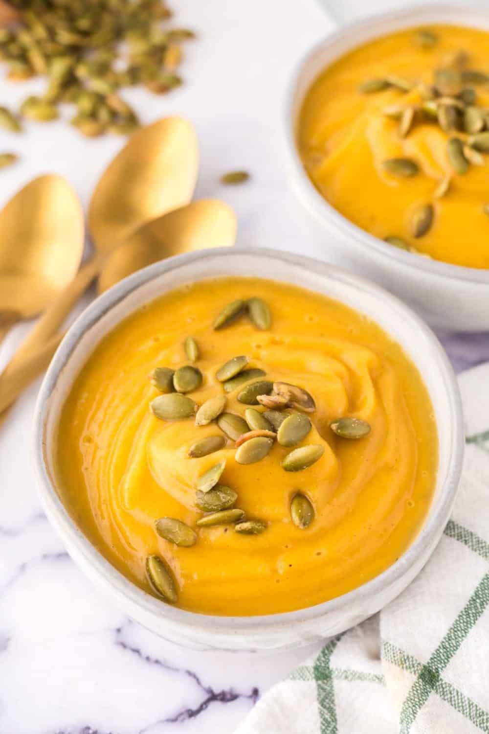 white serving bowls of roasted butternut squash soup with pumpkin seeds on top