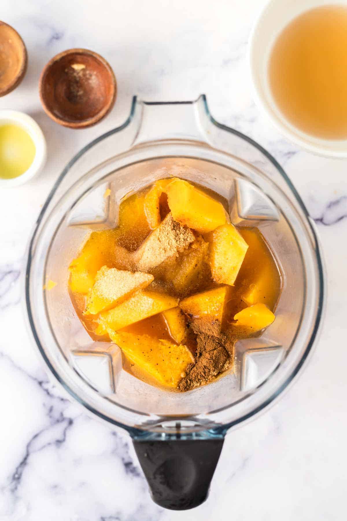 top view of a blender with spices and roasted butternut squash for soup