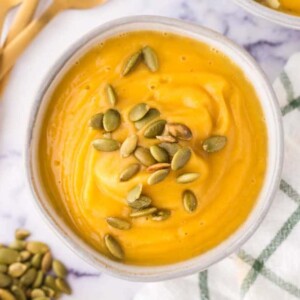 top view of a white bowl of roasted butternut squash soup with pumpkin seeds on top