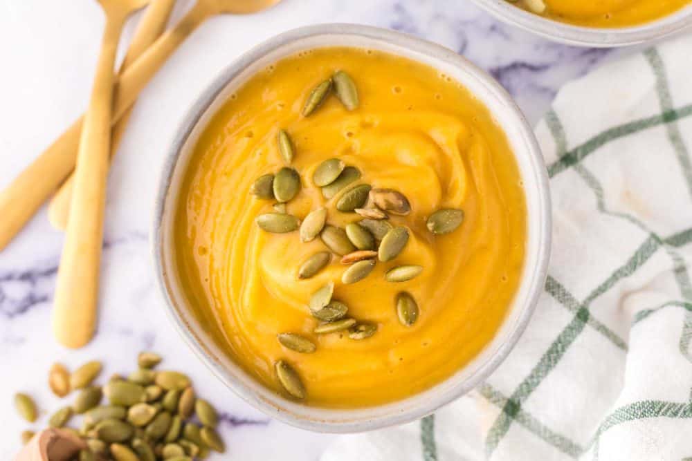 top view of a white bowl of roasted butternut squash soup with pumpkin seeds on top.