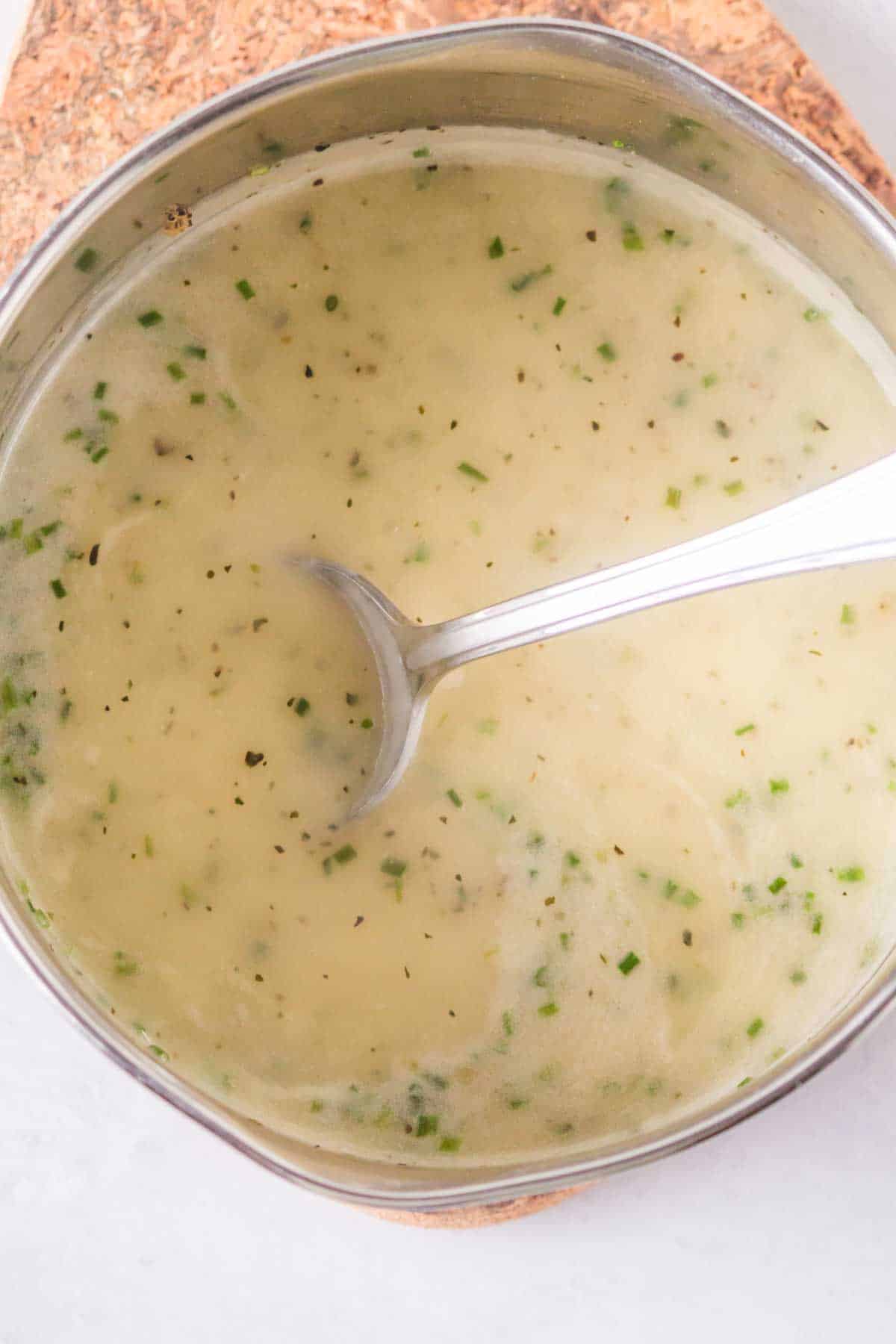 spoon in chicken gravy in a metal mixing bowl