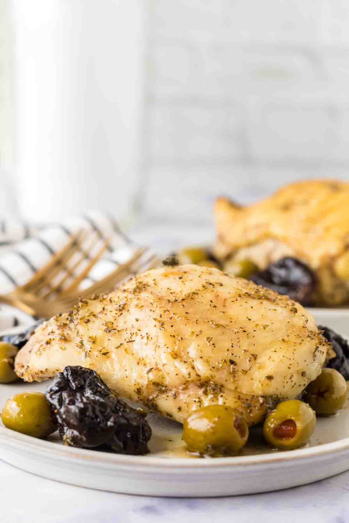 side view of a round white plate with chicken marbella recipe with dates and olives around