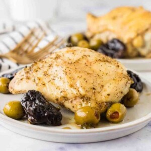 side view of a round white plate with chicken marbella recipe with dates and olives around