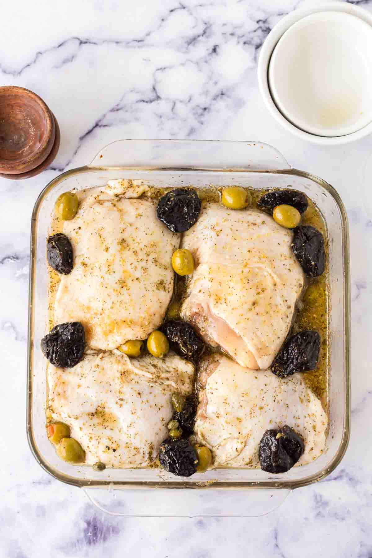 four breasts in a square casserole dish with chicken Marbella recipe inside