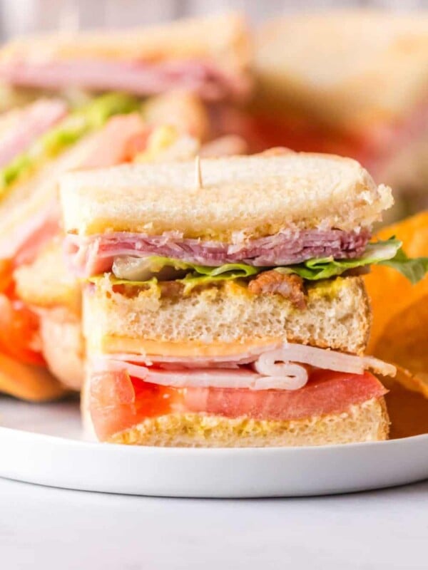 side view with a round white plate with a club sandwich on top with chips