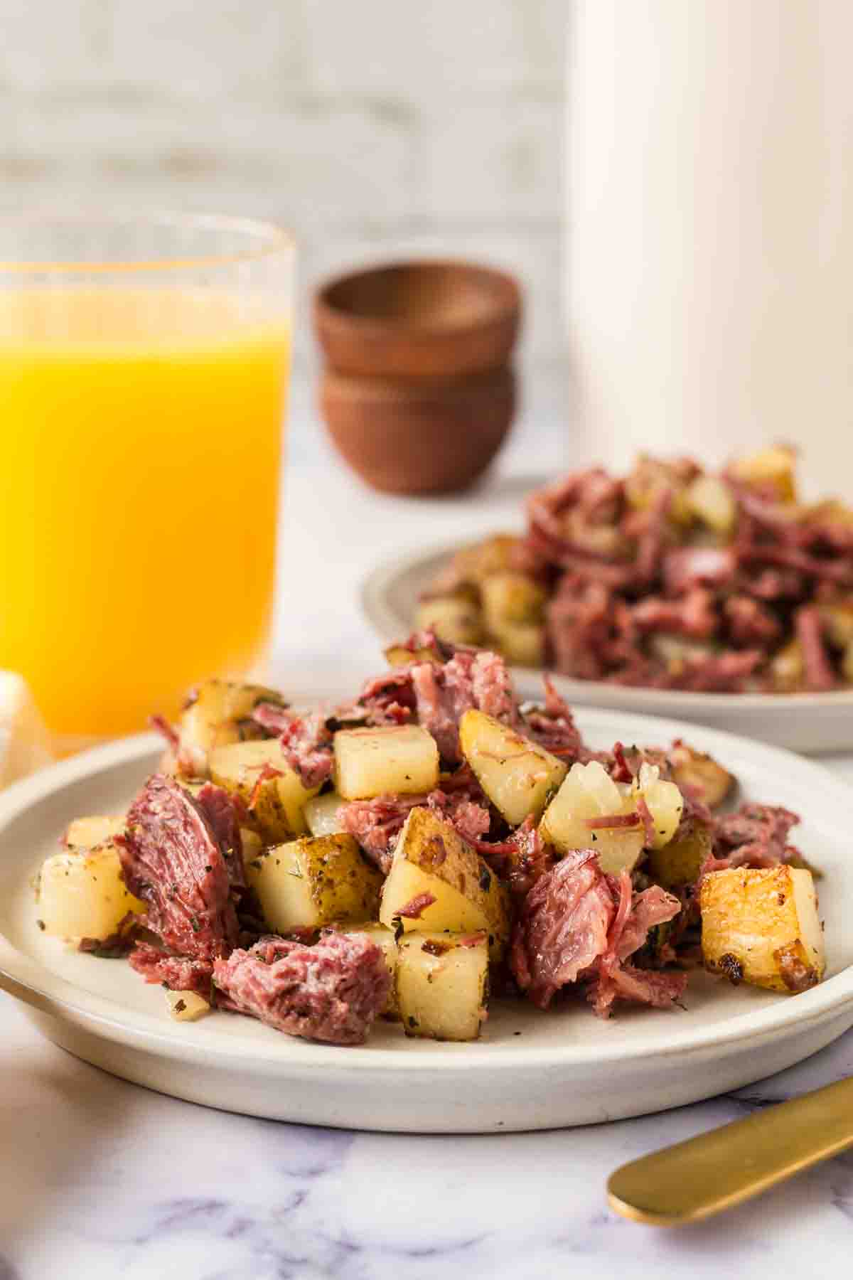 Corned beef hash served on a white plate with orange juice in a glass. 