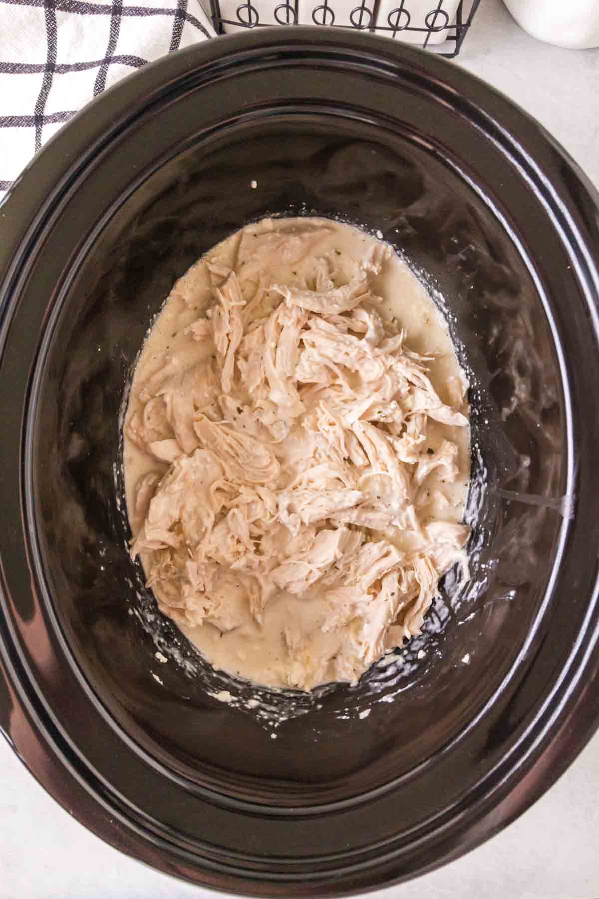 slow cooker with seasoned crack chicken inside shredded and sauced