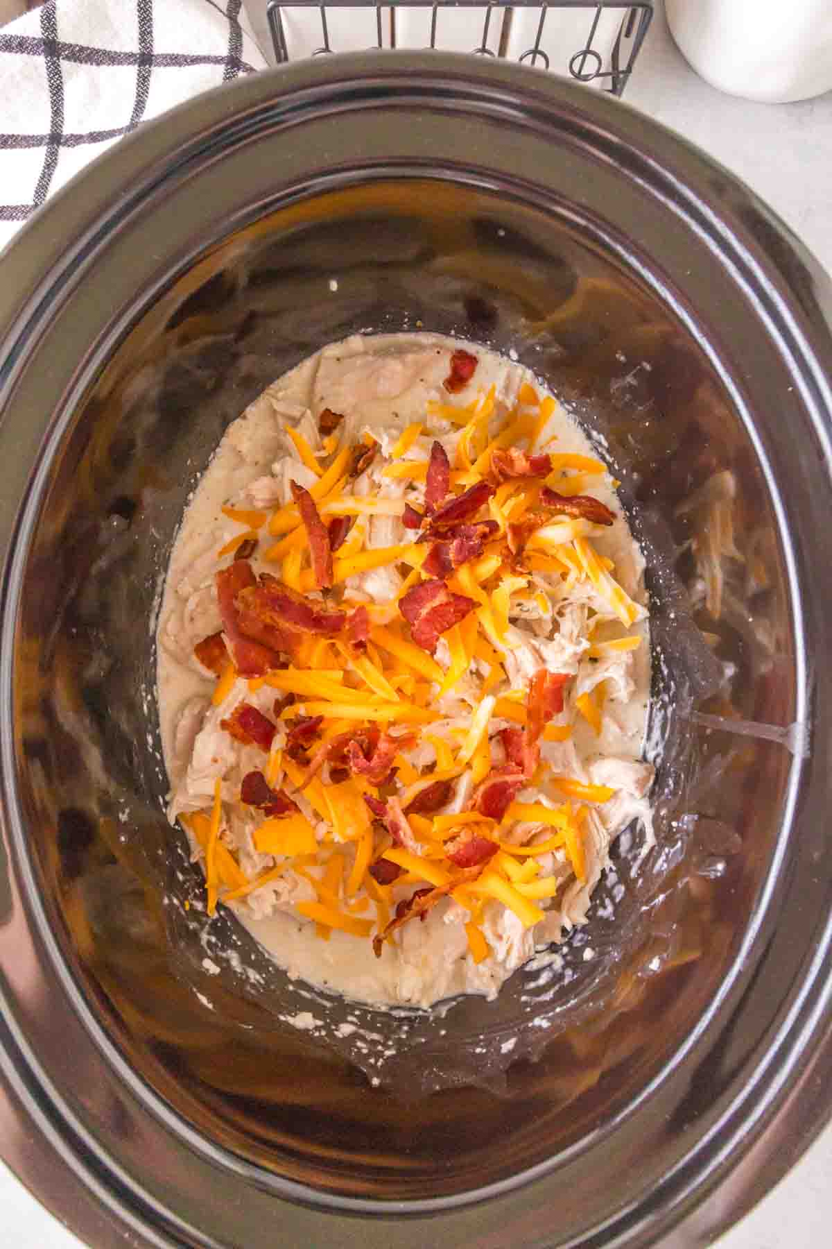 slow cooker with seasoned crack chicken inside shredded and sauced