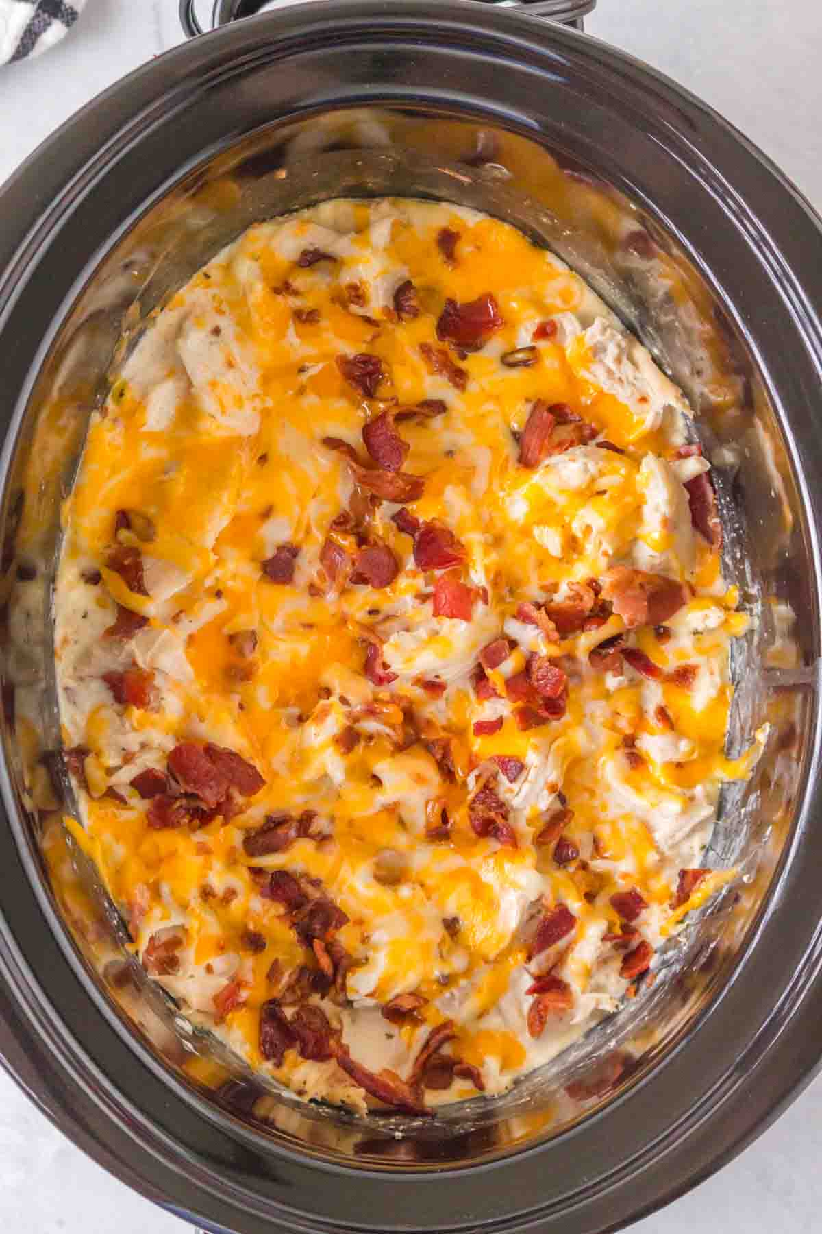 slow cooker with seasoned crack chicken inside shredded and sauced with melted cheese