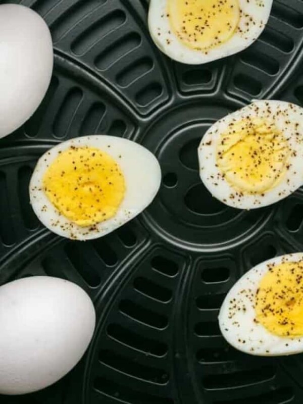 air fryer basket image up close with whole eggs and some hard boiled eggs seasoned and cut in half.