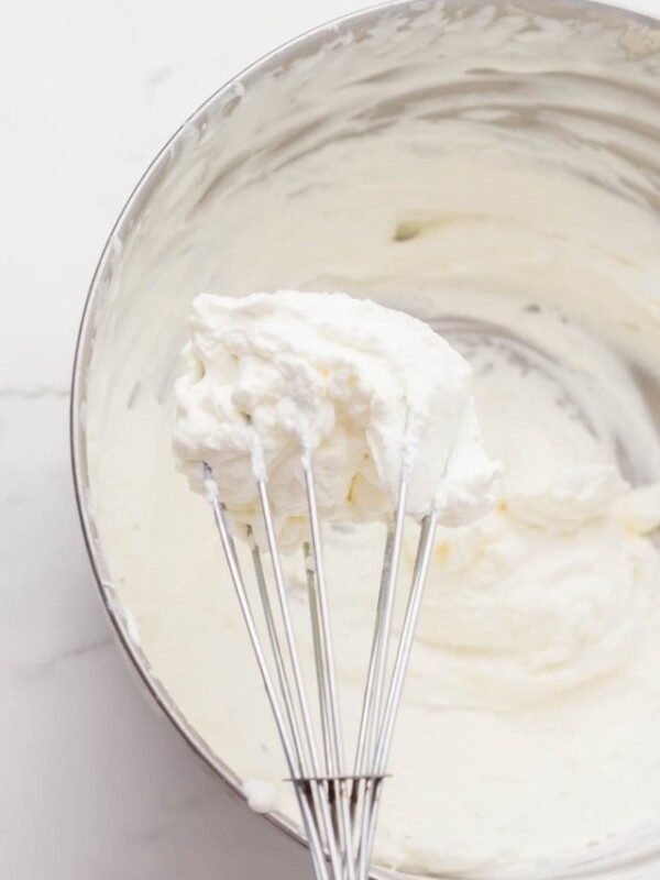 metal mixing bowl with whipping cream and a whisk inside.