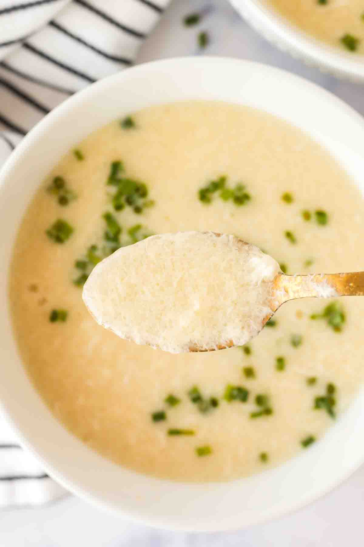 POV spoonful over egg drop soup in a white bowl with herbs on top