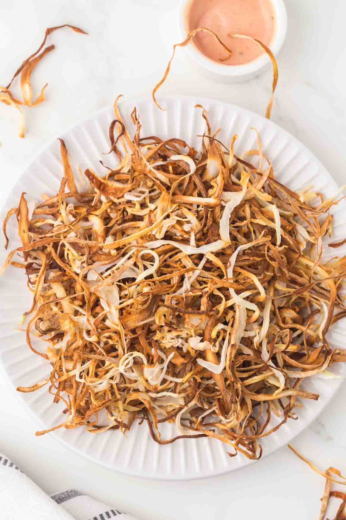 white plate with a nest of thinly sliced fried onions