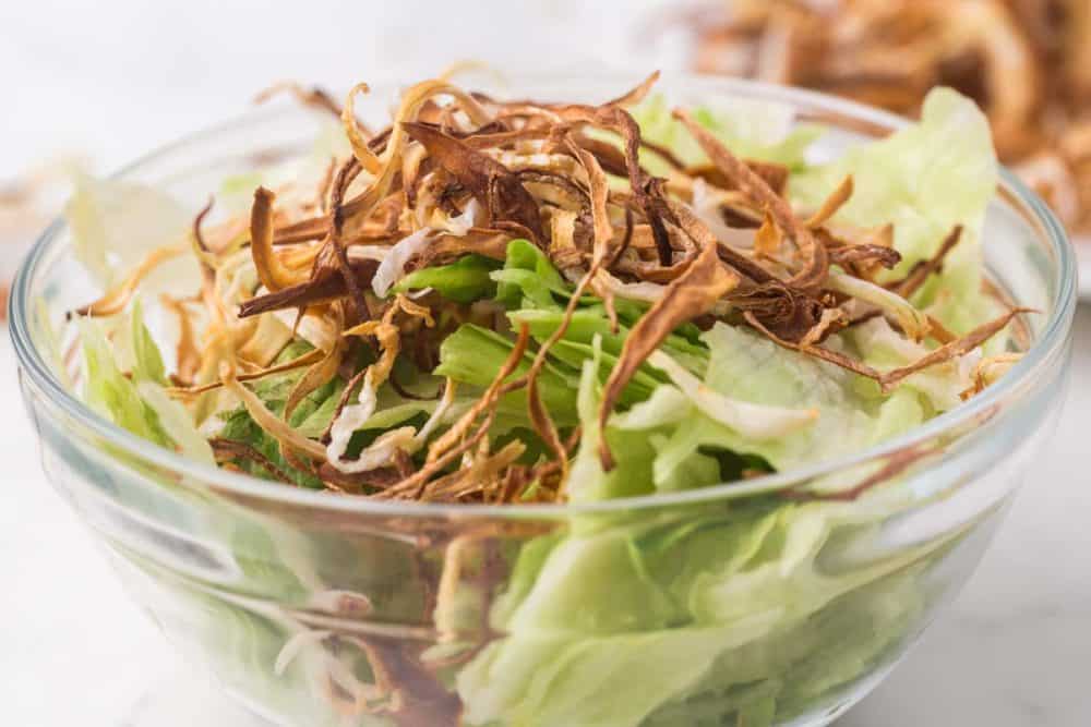 fried onion shreds over a clear bowl of lettuce