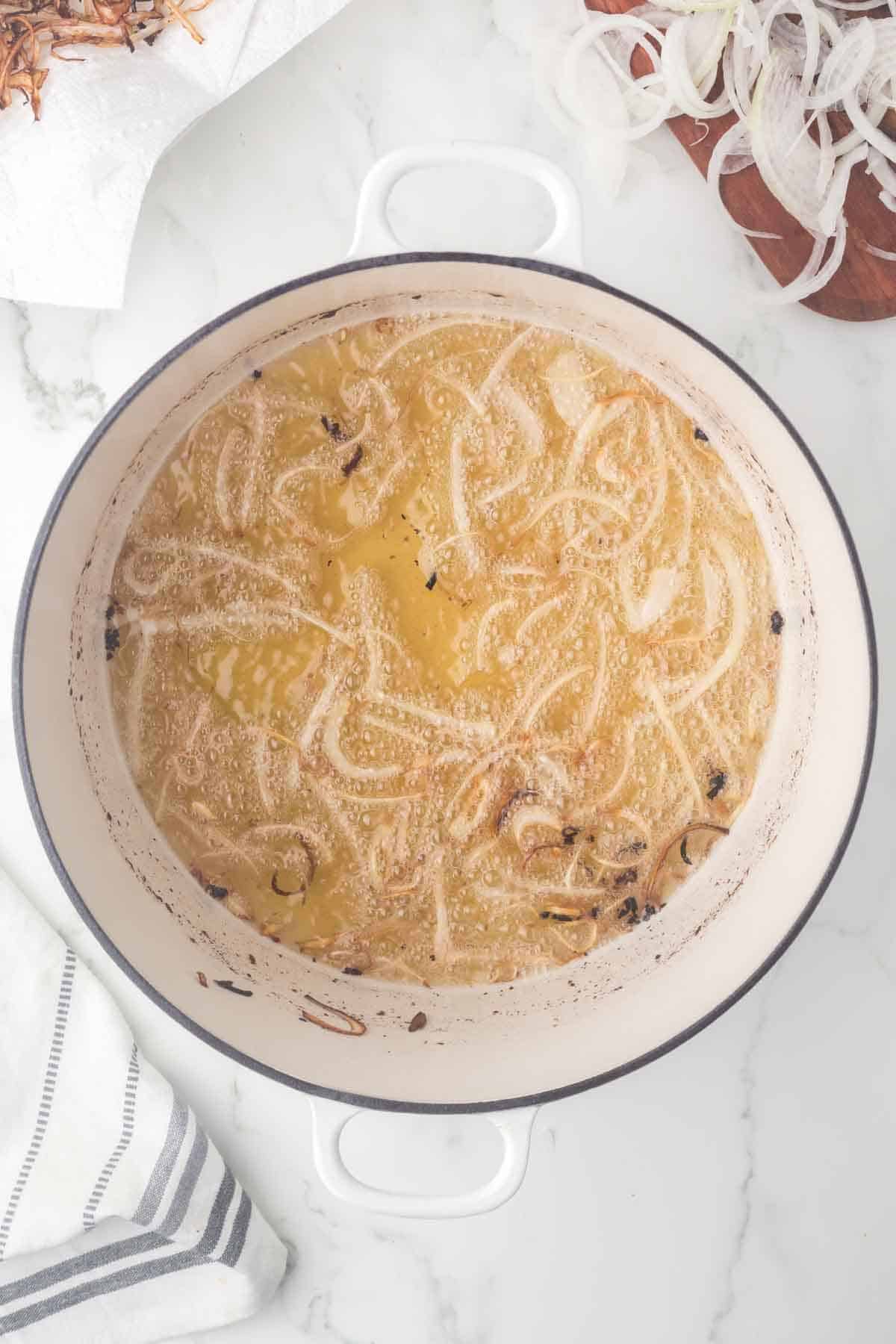 a deep pot with oil in it and frying small slices of onions
