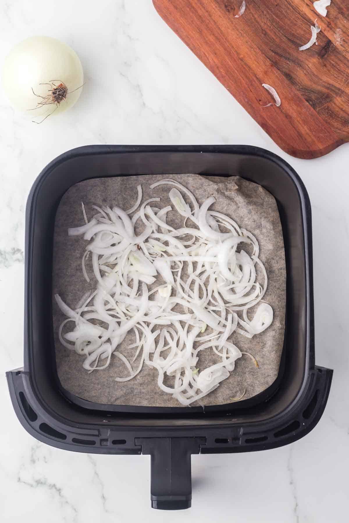 air fryer basket with small slices of white onions
