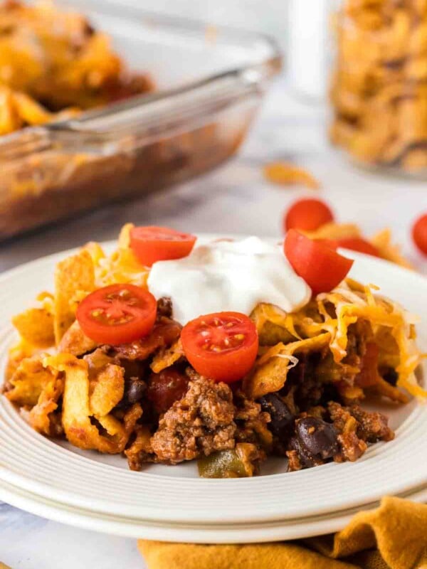 white dinner plate with frito pie with a dollop of sour cream and sliced cherry tomatoes on top