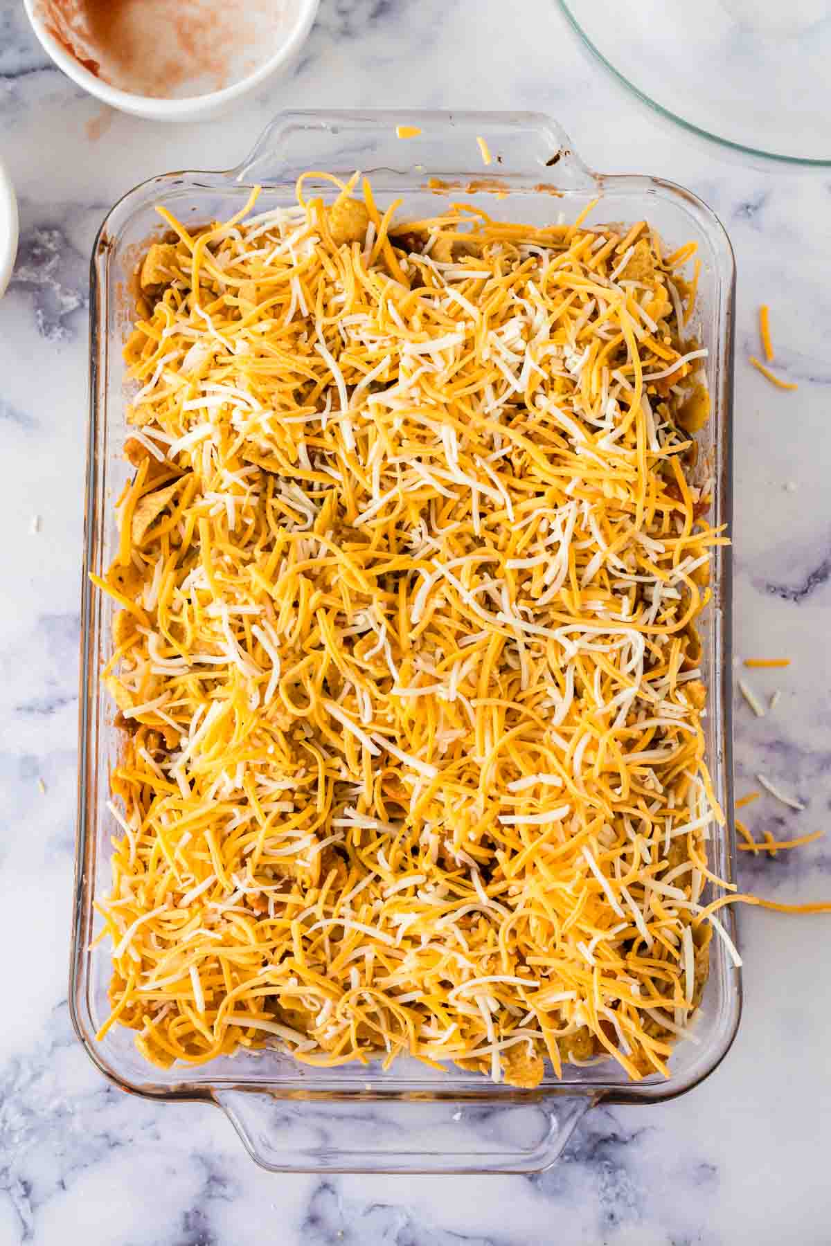 casserole dish with frito pie inside and cheese on top before melting