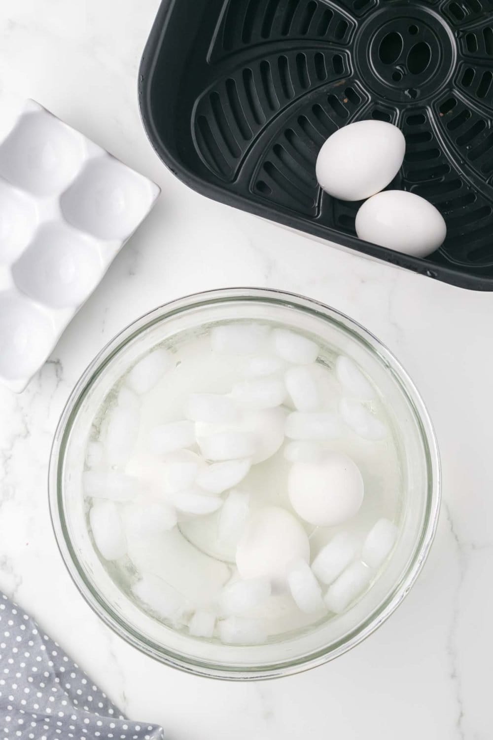 air fryer basket with whole eggs inside and a glass bowl of ice water