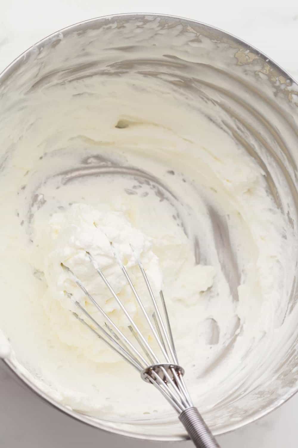 metal mixing bowl with whipping cream and a whisk inside