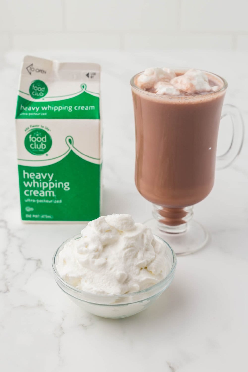 an image of a glass of coco a dish of whipped cream next to a carton of heavy whipping cream