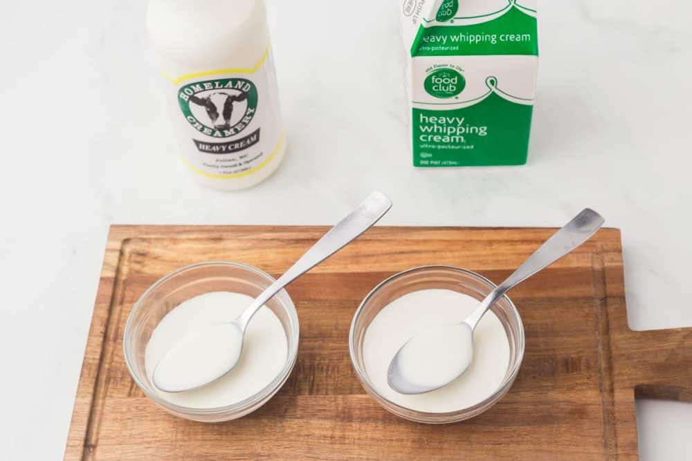 image of different cartons of cream and heavy whipping cream next to two small clear bowls with cream and a spoon in them over a wooden board