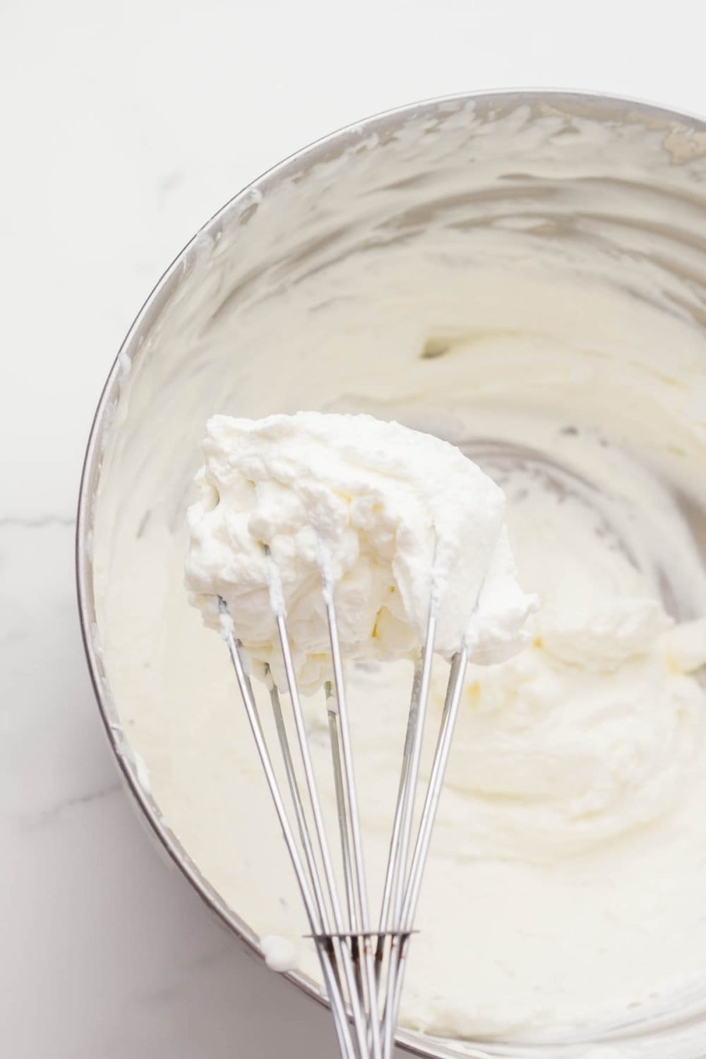 metal mixing bowl with whipping cream and a whisk inside