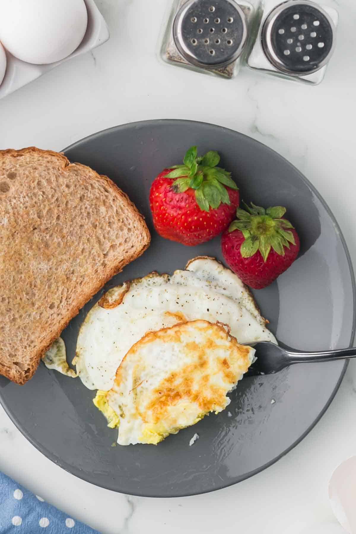 grey plate with toast and a fried egg on the side with strawberries