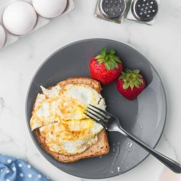 grey plate with toast and a fried egg on the top with strawberries on the side