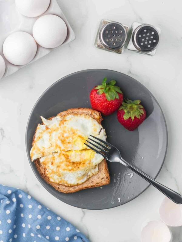 grey plate with toast and a fried egg on the top with strawberries on the side