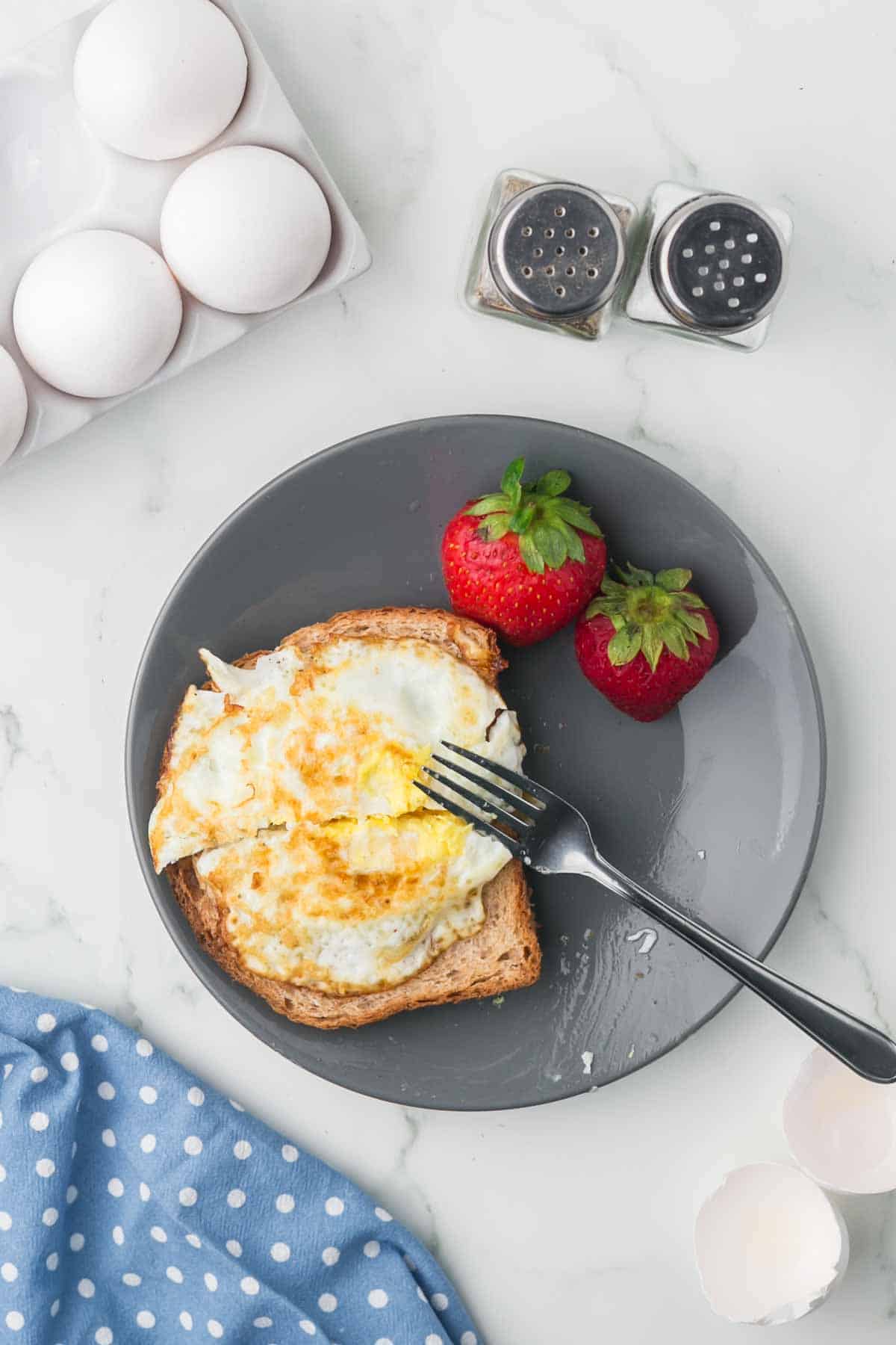 grey plate with toast and a fried egg on the top with strawberries on the side