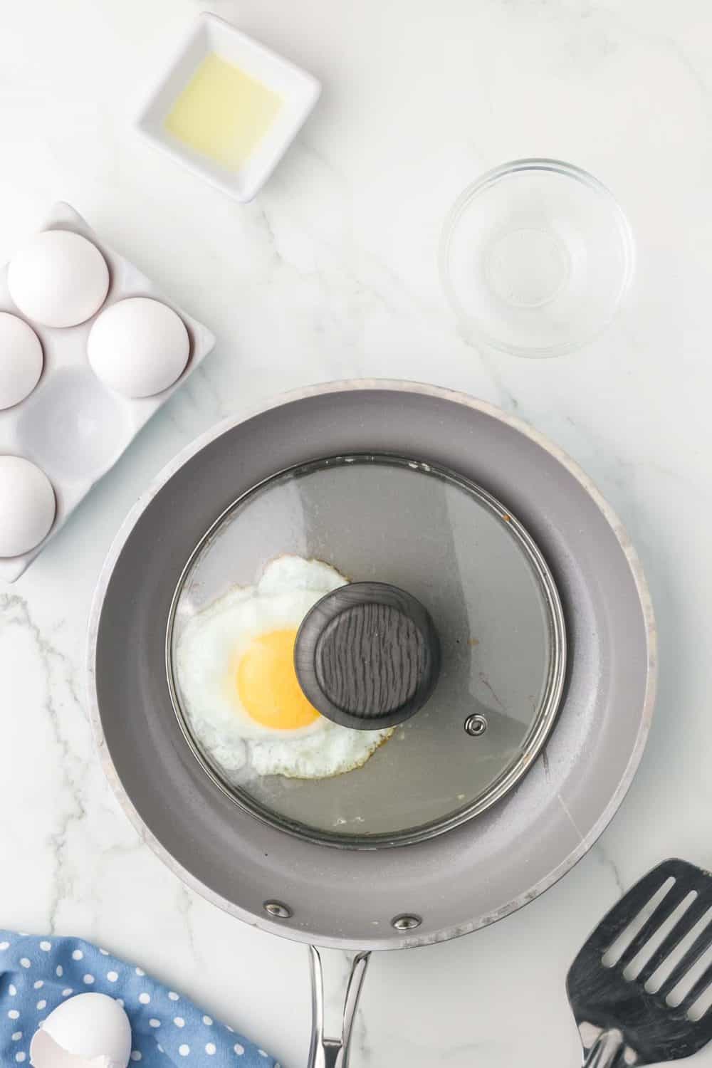sautéed pan with an egg cooking and a lid over it
