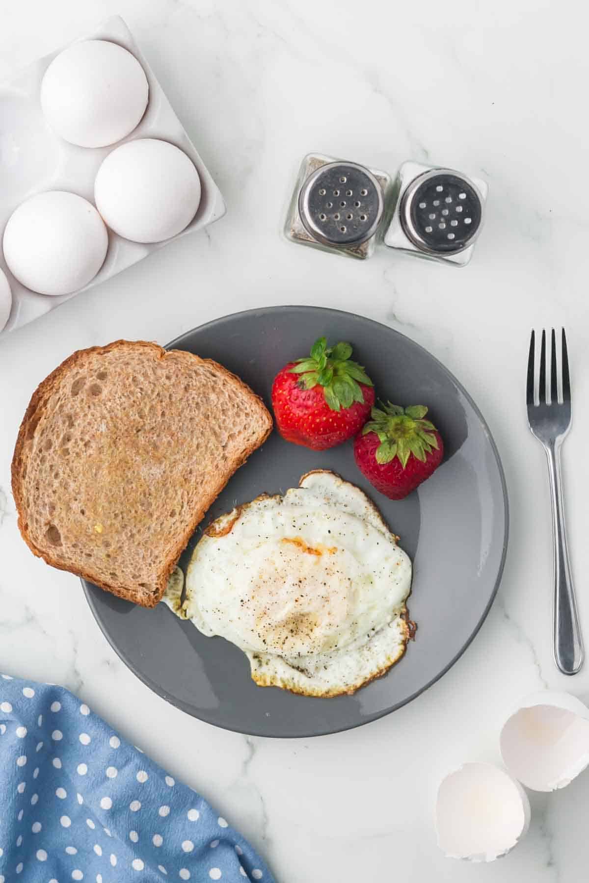 grey plate with toast and a fried egg on the side with strawberries