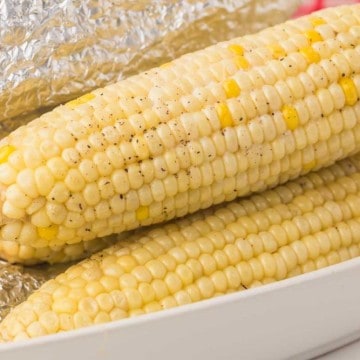 three stacked cooked and buttered corn on the cob in a dish lined with foil