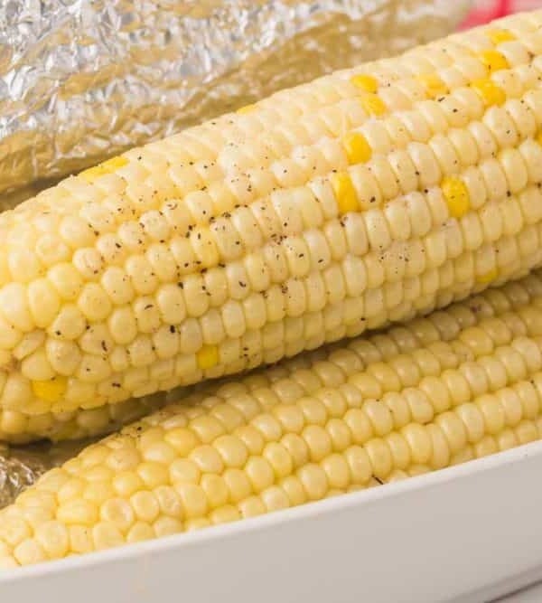 three stacked cooked and buttered corn on the cob in a dish lined with foil