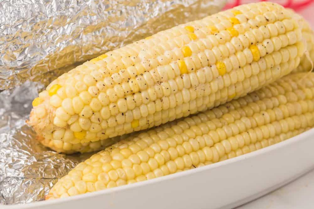 three stacked cooked and buttered corn on the cob in a dish lined with foil