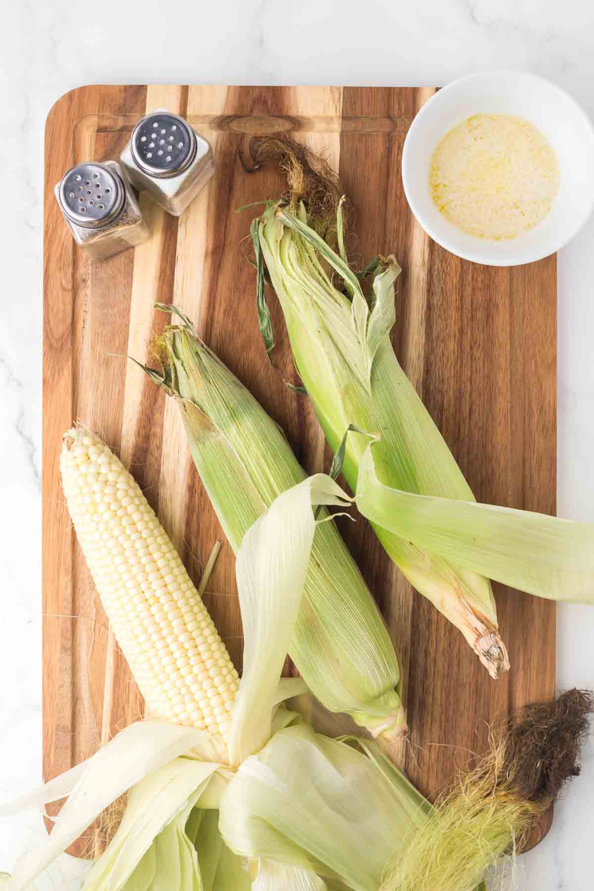 corn on the cob with the husk on, atop a wooden block