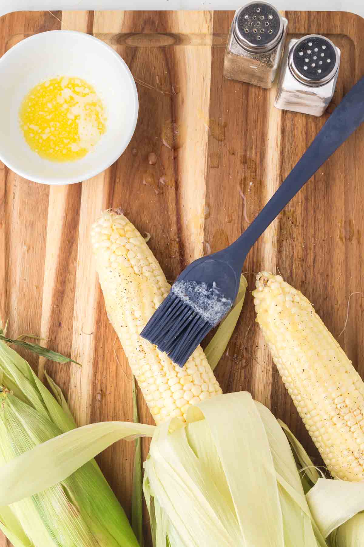 three pieces of corn on the cob with the husk pulled down and the corn lathered in buttered laying on a wooden board