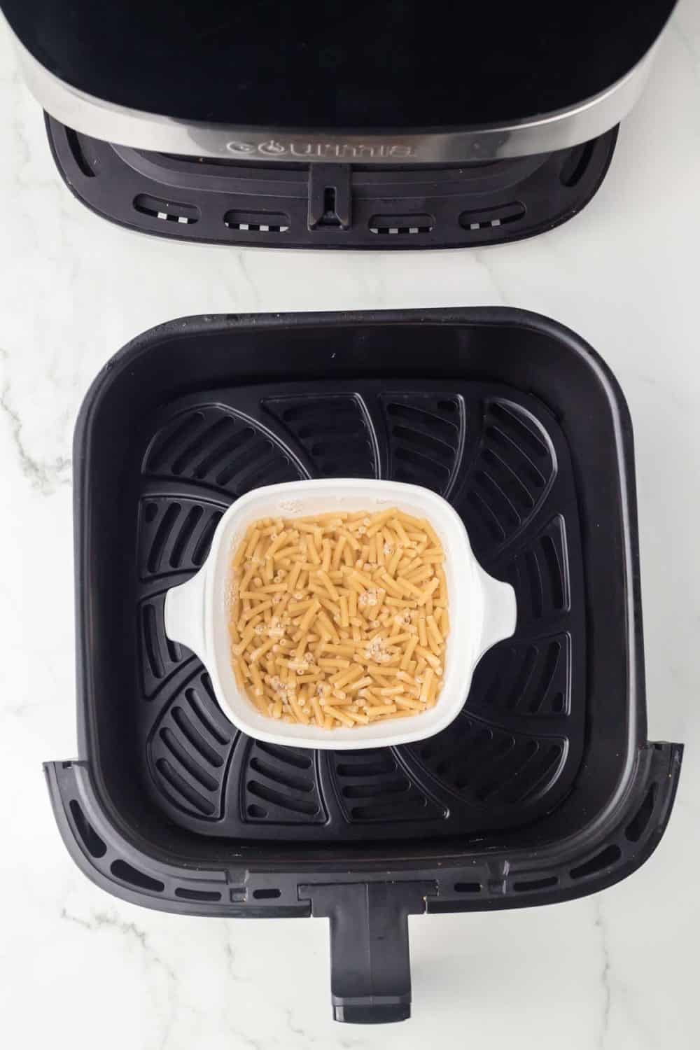 top view of an air fryer basket with a dish and raw pasta inside