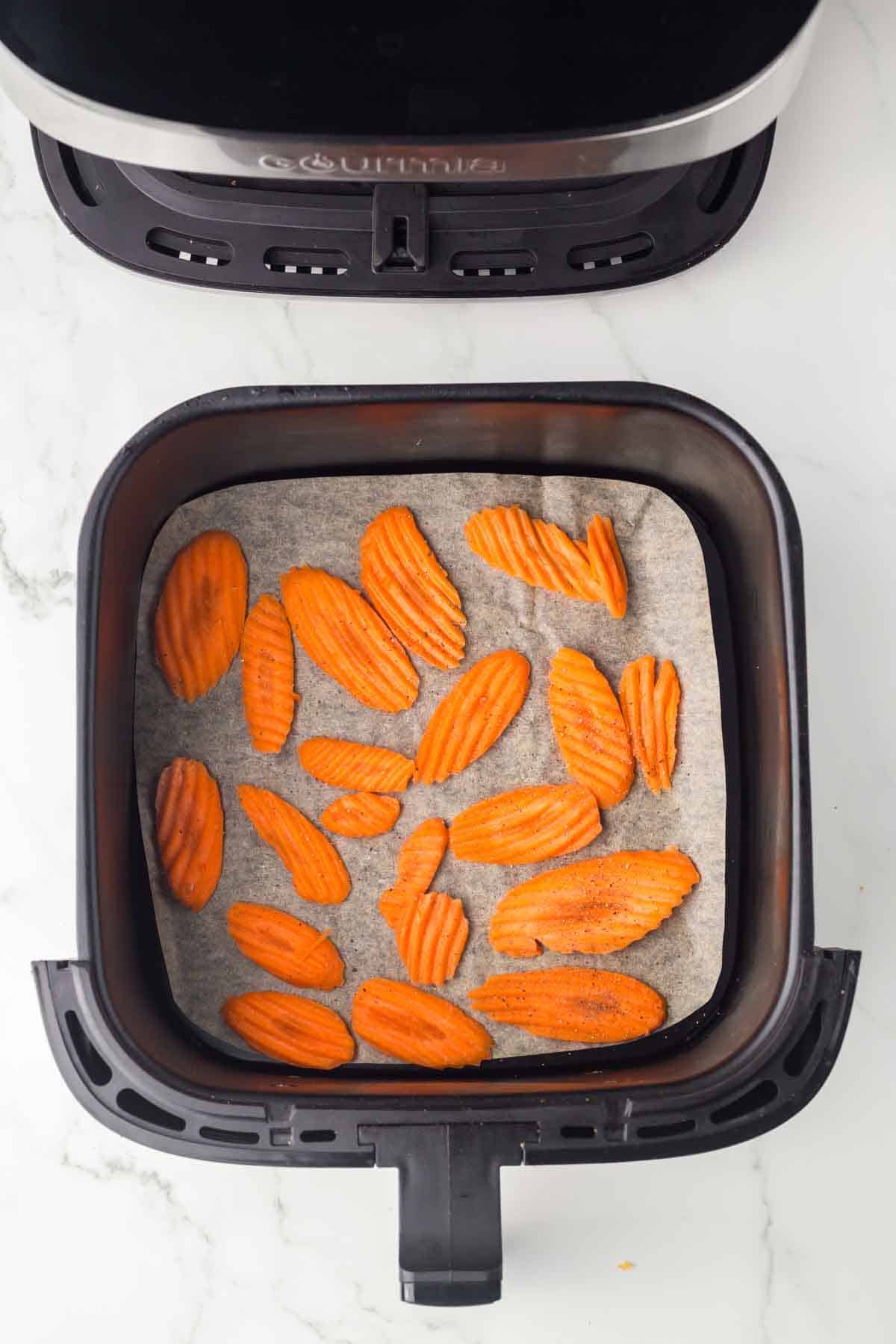 top view of an air fryer basket with slices of carrots on parchment paper