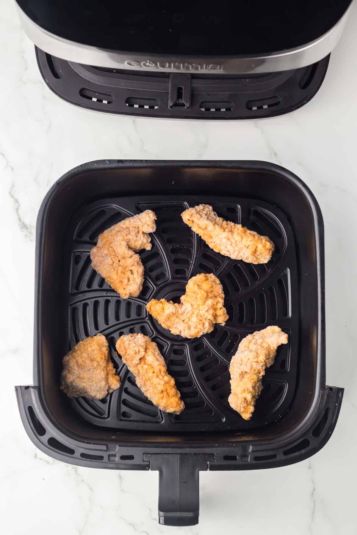 top view of an air fryer basket with chicken tenders inside