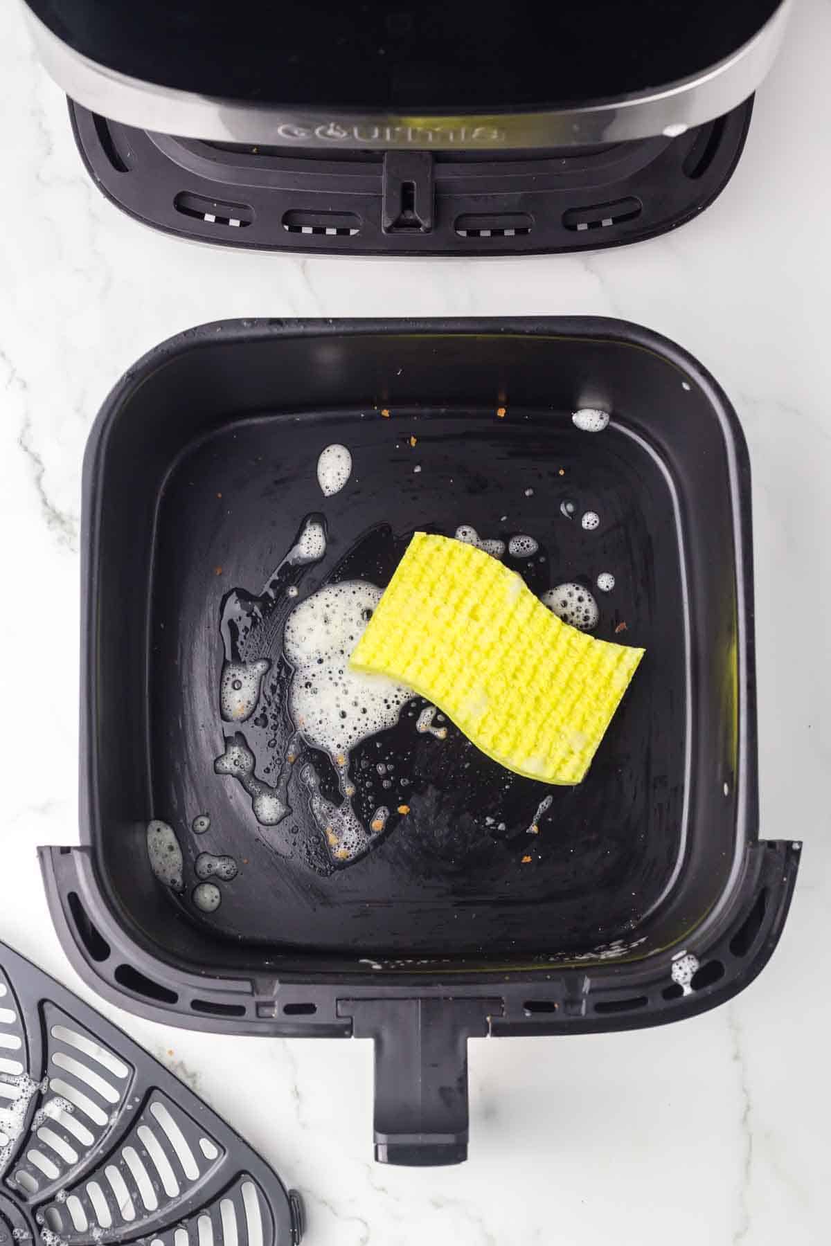 top view of an air fryer basket being cleaned with a sponge