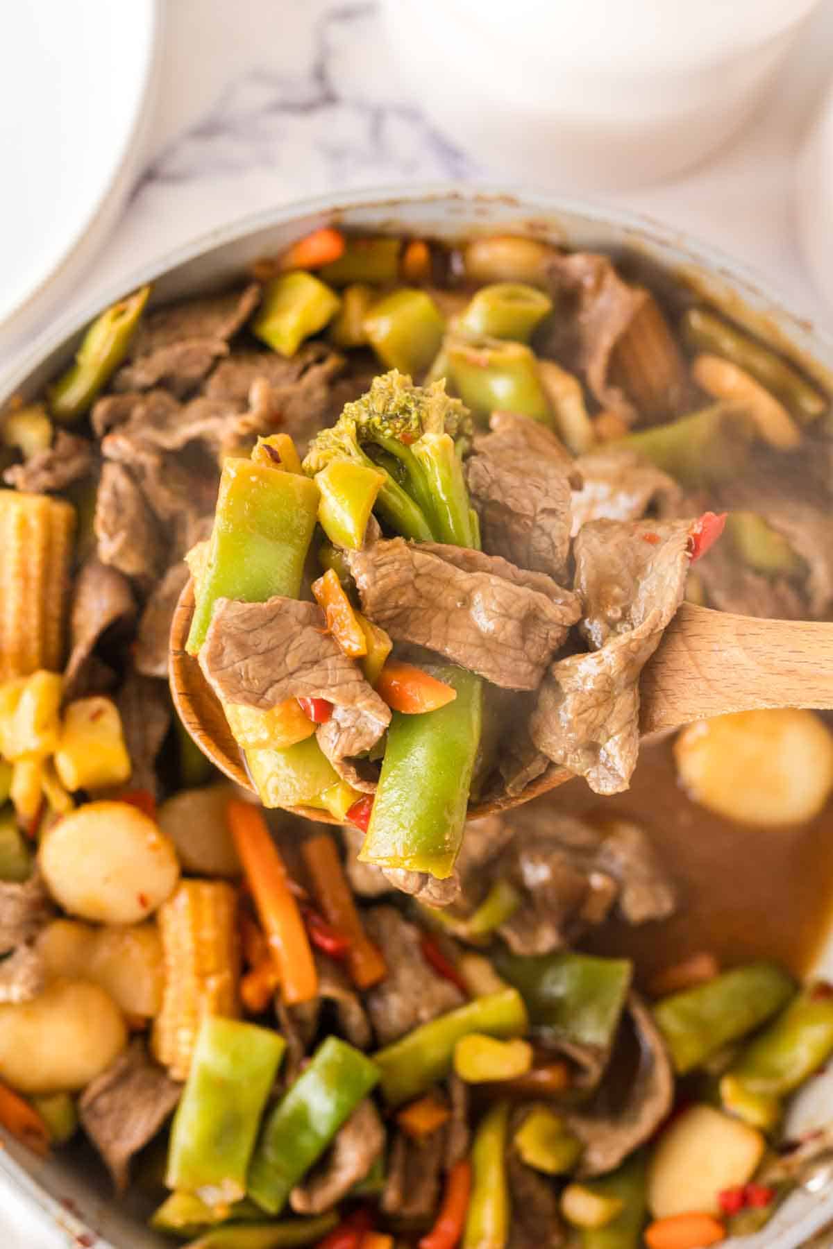 POV with a wooden spoon over a sauce pan with the cooked mix for the hunan beef recipe