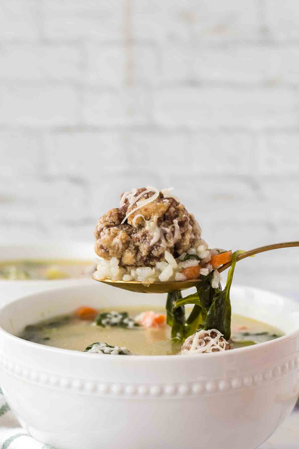POV side view of a spoonful of italian wedding soup over a white bowl