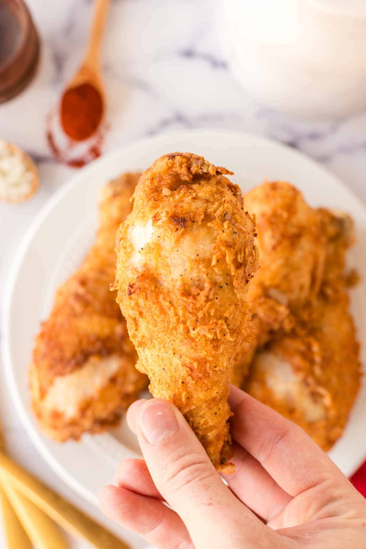 POV with a hand holding a leg of chicken over a white plate stacked with Louisiana chicken legs