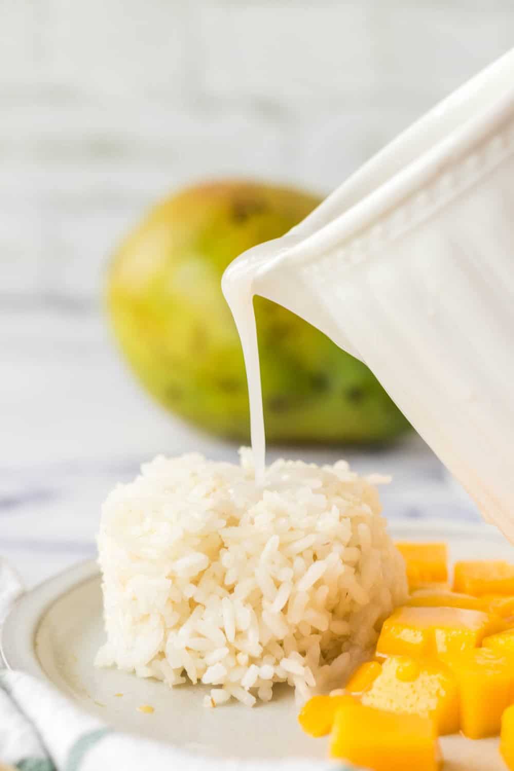 coconut milk being poured over mango sticky rice on a white plate