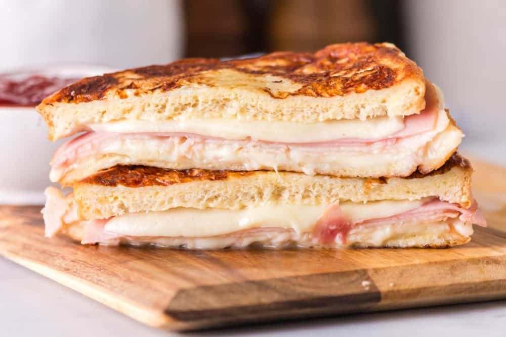 side view sliced in half of a grilled monte cristo sandwich dipped in eggs and grilled then displayed on a wood block