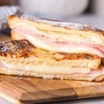 side view sliced in half of a grilled monte cristo sandwich dipped in eggs and grilled then displayed on a wood block