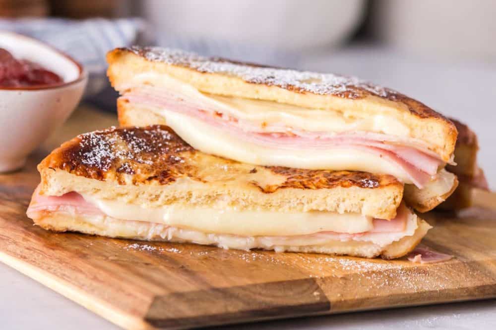 side view sliced in half of a grilled monte cristo sandwich dipped in eggs and grilled then displayed on a wood block